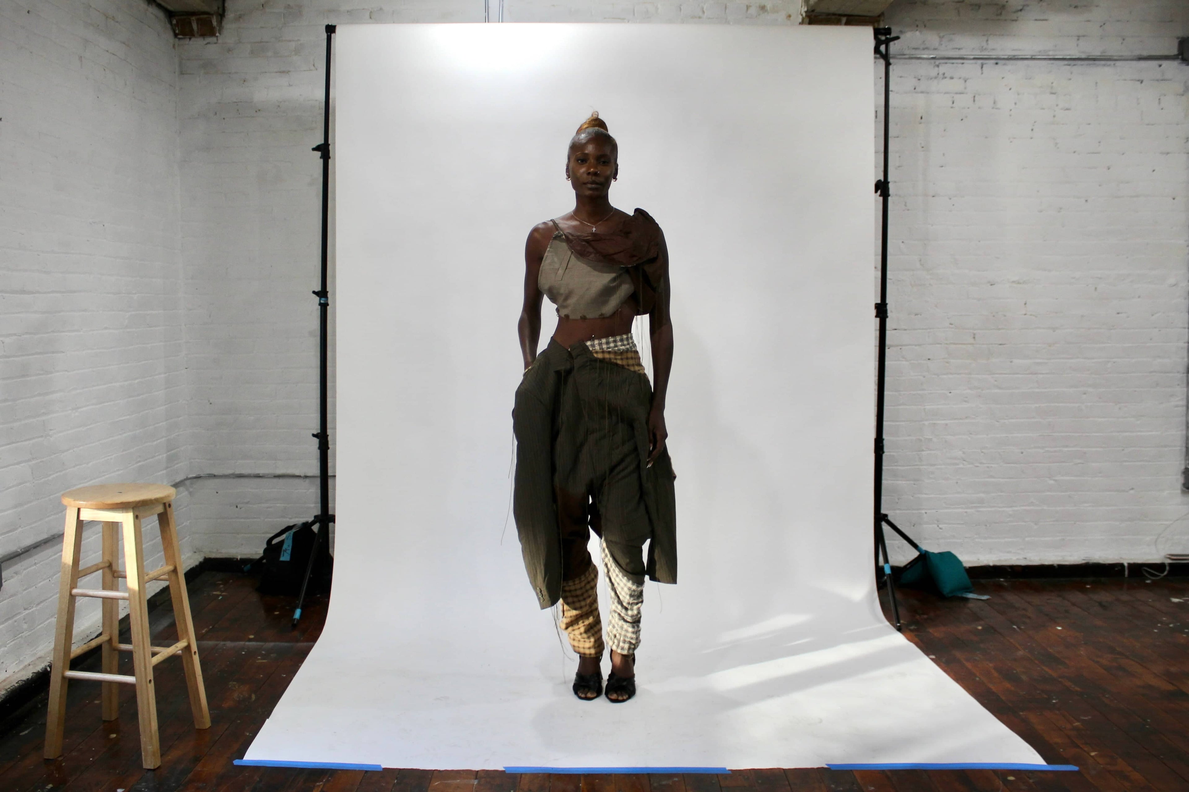 Model wearing deconstructed suit-blazer pants and asymmetrical top in rich brown tones from the Corii Burns MHII Collection during New York Fashion Week studio fitting.