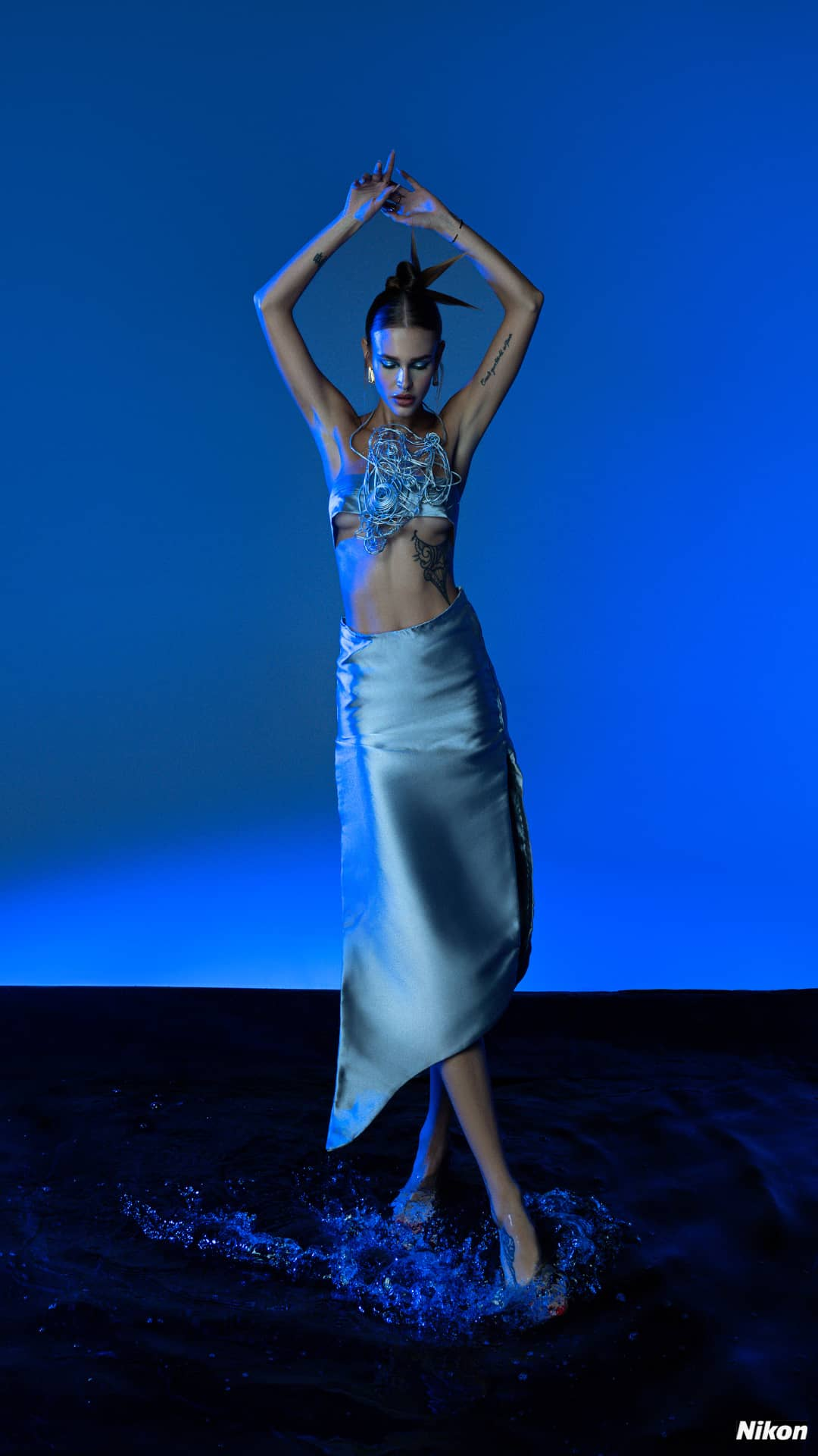 Fashion model Eva Minaeva showcasing Corii Burns silver Sante Mentale luxury designer brazier and necklace on a vivid blue backdrop